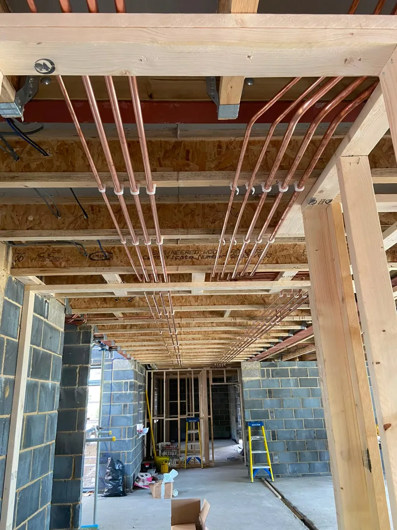 Parallel copper heating pipes clipped beneath timber joists