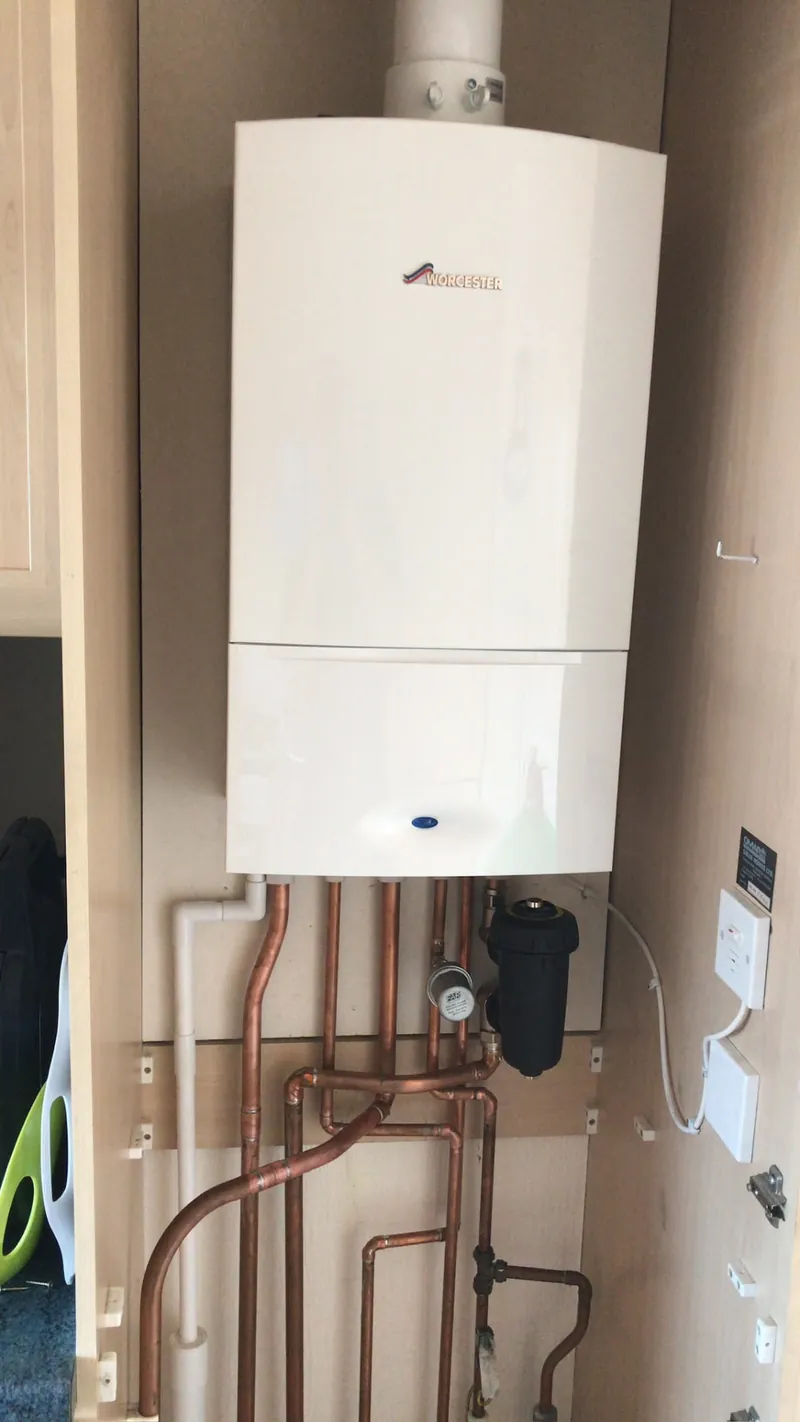Worcester boiler with filter and copper pipes inside a kitchen cabinet