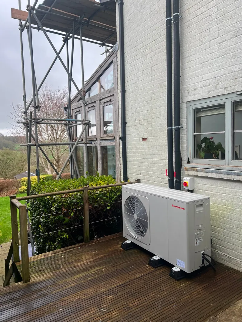 Air source heat pump unit fitted on timber decking beside a rendered house