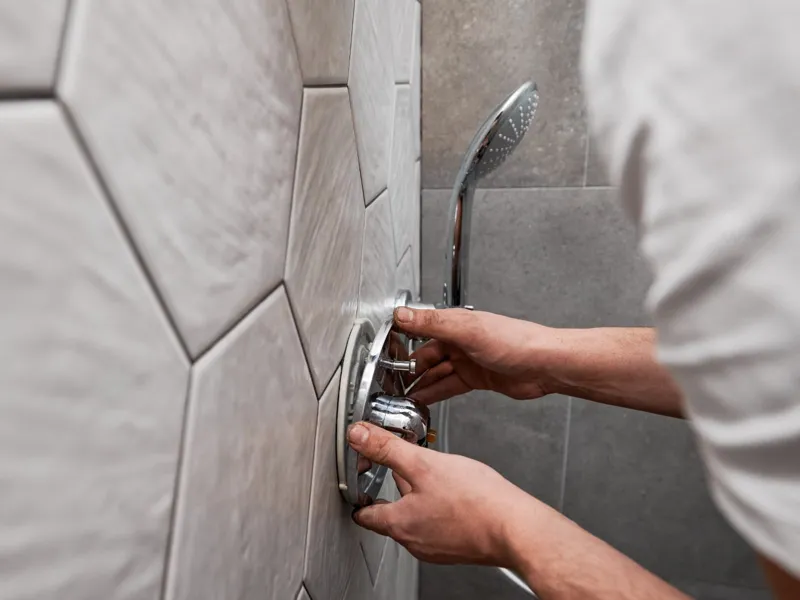 Engineer fitting a chrome thermostatic shower valve on a tiled wall